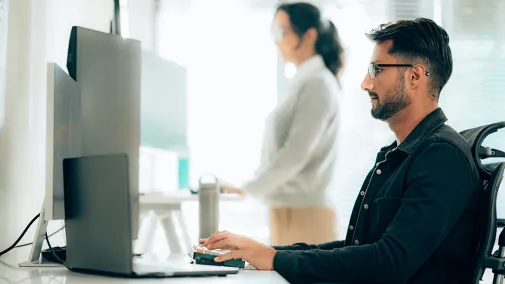 Mann sitzt am Computer in einem Büro und schaut auf den Monitor während er auf der Tastatur tippt.