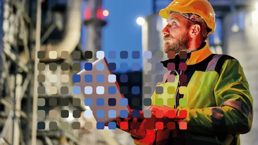 A technician wearing a safety helmet works on a laptop at night in an industrial plant