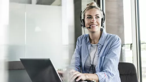Frau am Computer mit Telefon und Headset im Büro Frau am Computer mit Telefon und Headset im Büro