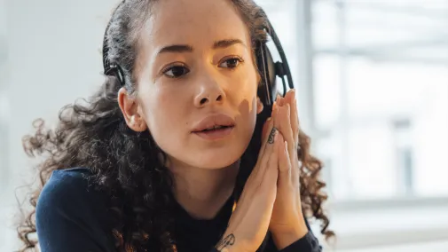 Frau mit Kopfhörern schaut konzertiert auf ihren Laptop.