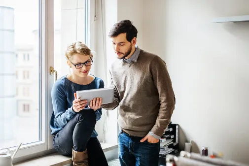 A man and a woman are viewing a website on a tablet.