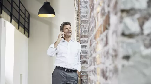 Mann steht mit Smartphone telefonierend im Büro Mann steht mit Smartphone telefonierend im Büro