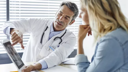 Arzt zeigt einer Patientin Röntgenaufnahmen auf einem Tablet Arzt zeigt einer Patientin Röntgenaufnahmen auf einem Tablet