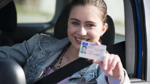 Woman sitting at the wheel and showing her driving licence.
