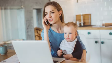 Frau sitzt mit Kind am Computer mit Handy zu Hause