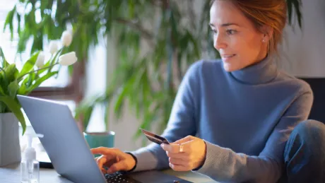 Frau mit Notebook und Kreditkarte am Tisch zu Hause