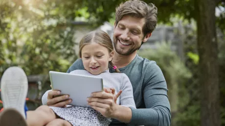 Mann und Kind sitzen mit Tablet draussen