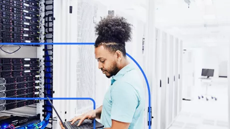 A man is standing in front of a notebook in the server room.