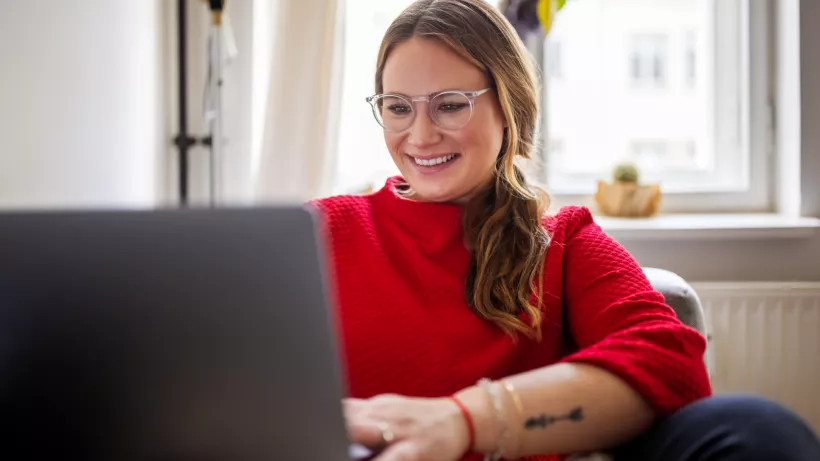 Frau sitzt mit Notebook zu Hause auf dem Sofa